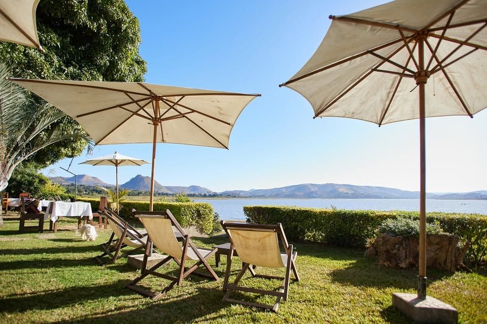 Outdoor seating area with umbrellas and deck chairs overlooking a serene lake and distant mountains.